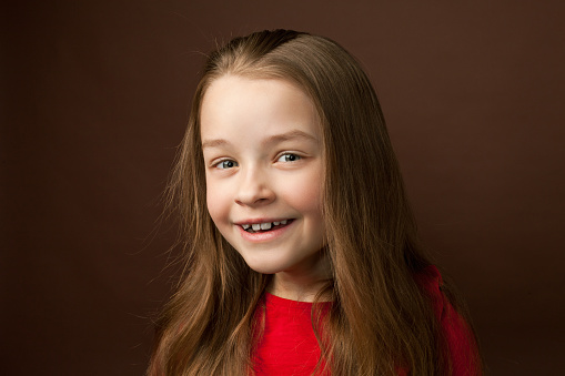 close-up studio portrait of a 9 year old girl with long brown hair in a red dress on a brown background