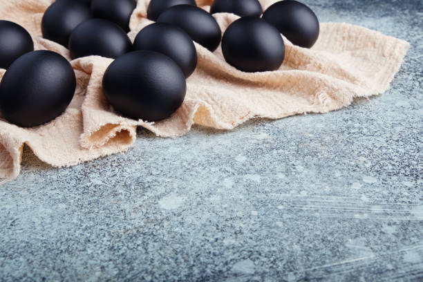istock Black Easter eggs on a linen napkin on a blue texture table. Easter celebration concept. 1215502542