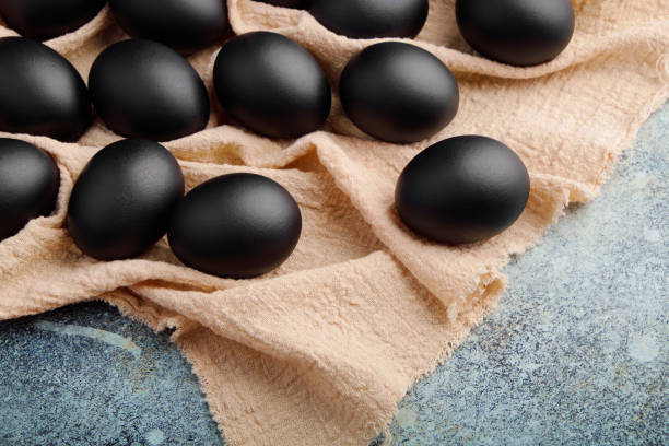 istock Black Easter eggs on a linen napkin on a blue texture table. Easter celebration concept. 1215502552