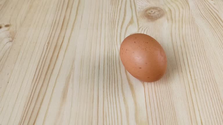 Brown chicken egg spins on wooden table