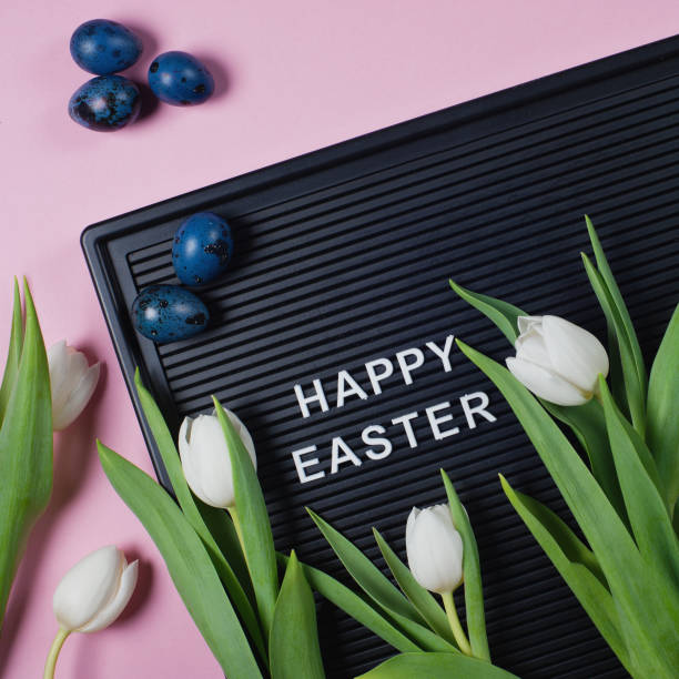 istock Happy Easter - text on black letter board with white tulips and blue colored eggs on pink background. 1215511251