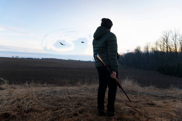 A teenaged hunter standing on a hill looking over farm fields at dusk