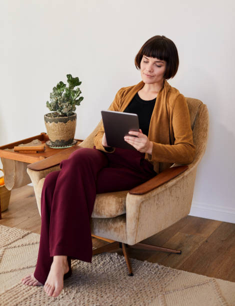 istock Smiling young woman sitting on a chair using a digital tablet 1215514139
