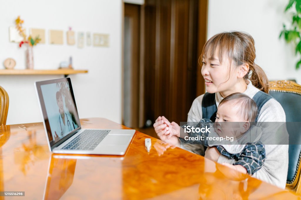 Mother with her baby video calling doctor from home A mother with her baby is video calling a doctor on a laptop from home. Telemedicine Stock Photo