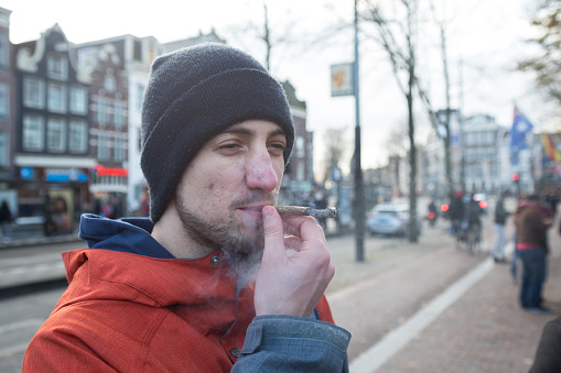 A young man smokes a cigarette with marijuana on the street of Amsterdam.