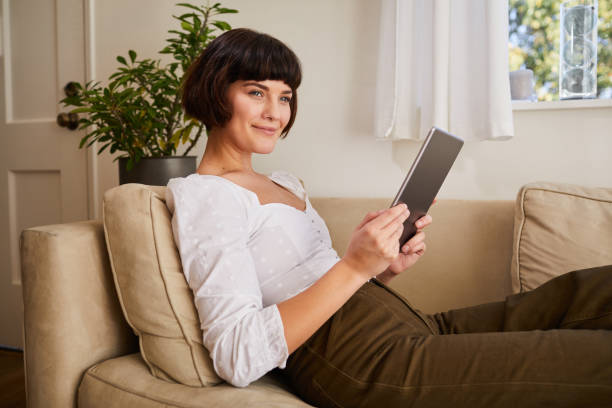 istock Smiling woman sitting on her sofa at home using a digital tablet 1215521398
