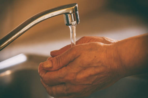 istock Senior washing hands under flowing tap water 1215530429