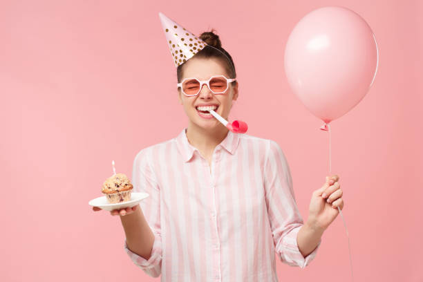 happy birhday girl celebrating, holding air balloon and cake, blowing whistle, isolated on pastel pink studio background - birthday party adult women imagens e fotografias de stock