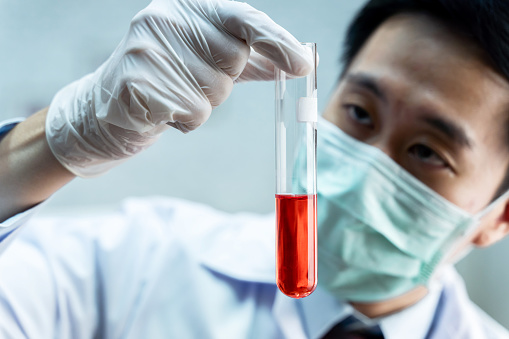 Close-up of Asian male scientist in white uniform holding laboratory flask with red chemical solution. Chemistry, Science, Biological, Toxicology, Research and Development concept