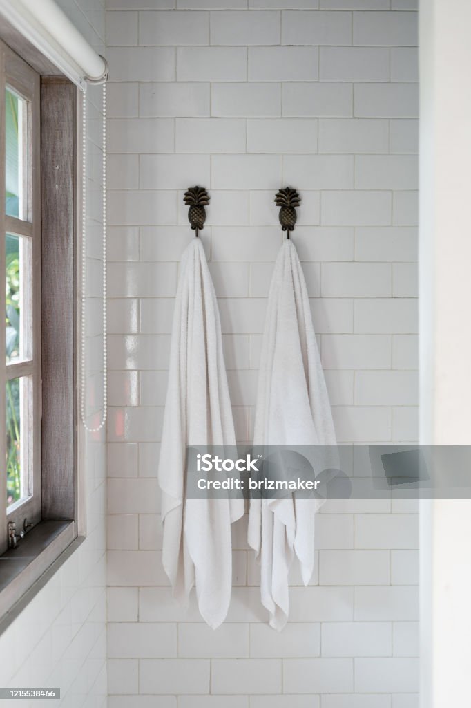 Two dry, clean and fresh towel on wall hanger in bathroom Vertical photo of two dry, clean and fresh towel on wall hanger in bright tiller bathroom with wooden frame window Towel Stock Photo