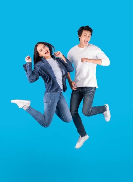 青い背景の上に幸せと楽しさでジャンプ若いアジアのカップルの男女 - healthy lifestyle women jumping happiness ストックフォトと画像