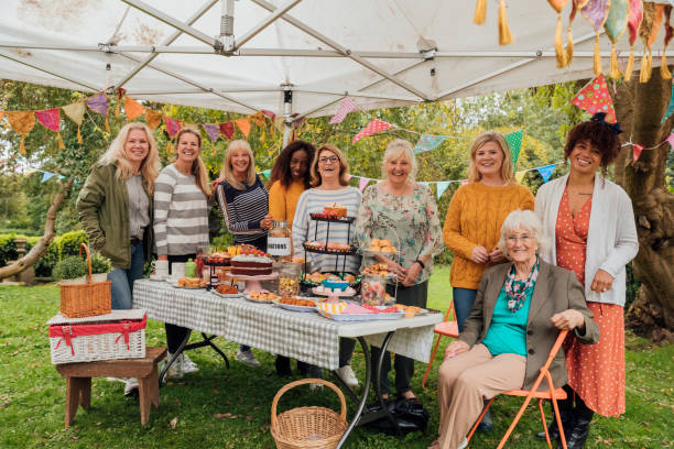 Cake Ladies A group of multi ethnic females stand in the garden around a cake stall. They are all smiling and looking at the camera. There is colorful bunting hanging from above inside the canopy. fall picnic table stock pictures, royalty-free photos & images