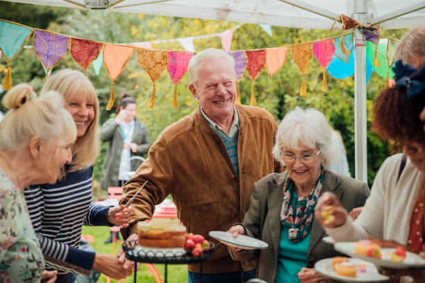 Seniors Enjoying Cake A group of seniors stand helping themselves to cakes in a garden, enjoying afternoon tea whilst chatting to eachother. There is colorful bunting hanging from above. fete stock pictures, royalty-free photos & images