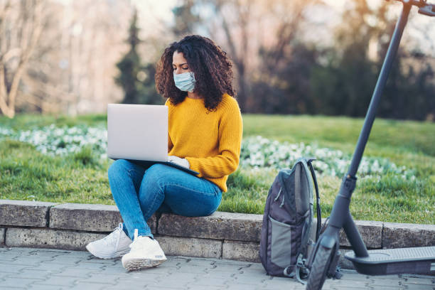 Woman working in the park during coronavirus social isolation Woman wearing a face mask working on a laptop outdoors in a park epidemiology student stock pictures, royalty-free photos & images
