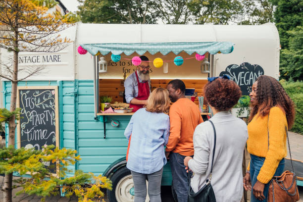 Food Truck Outside a serving hatch to a pretty painted food truck where a hipster guy is serving and chatting to a multi ethnic group of adults. Colorful bunting hangs from the canopy and surrounds the painted truck. fete stock pictures, royalty-free photos & images