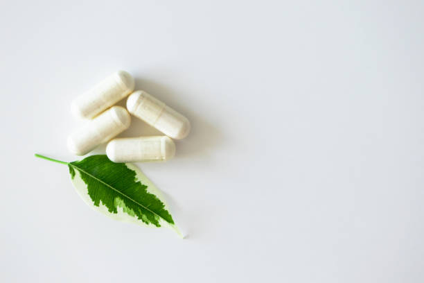istock Pill capsules heap and plant leaf on white background with copy space, top view. Concept alternative medicine. Natural immune defense. Vitamins and minerals 1215544444