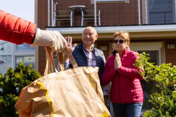 gratitude, thank you neighbor for supporting us during covid-19 shallow focus on hand with gloves bringing paper bag with food for thankful senior couple in their garden staying at home during coronavirus pandemic crisis curfew stock pictures, royalty-free photos & images