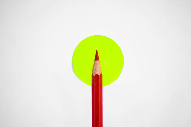 istock Single red pencil placed over a small yellow circle middle of a empty white background 1215549385