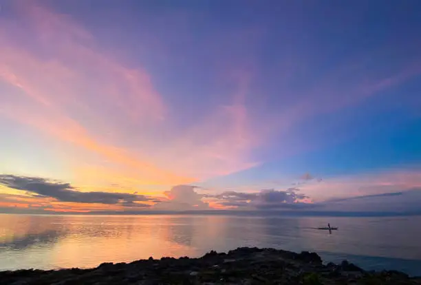 The magical landscape of incredibly beautiful sunset, dawn. Man sailing in a boat in the sea. Blue sky on the horizon with colored clouds. Rocky shore