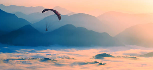 Paraglide silhouette flying over the misty mountain valley Paraglide silhouette flying over the misty mountain valley in a light of sunrise. airfoil photos stock pictures, royalty-free photos & images