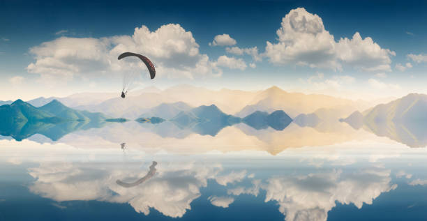 Flying paraglide silhouette over the extensive smooth water surface of a mountain lake, reflected in water