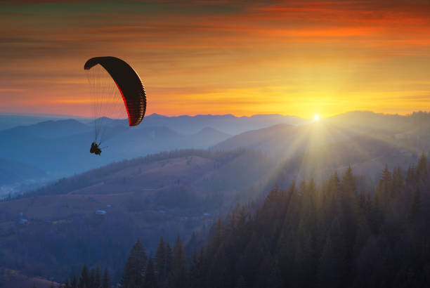 Paraglider silhouette flying in a light of colorful sunrise Paraglider silhouette flying in a light of colorful sunrise in a Carpathian mountain valley. Majestic landscape. Ukraine, Europe airfoil photos stock pictures, royalty-free photos & images