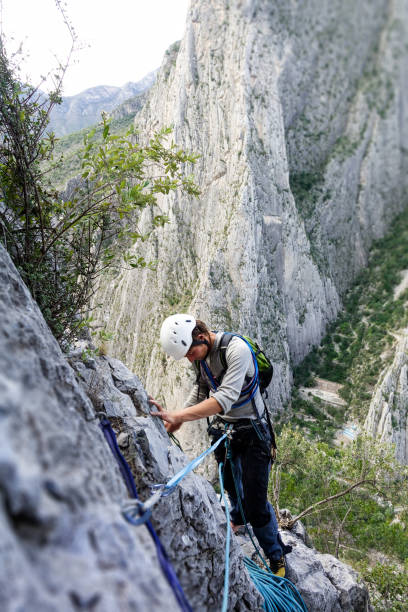 le jeune homme grimpe à potrero de chico au mexique, vérifiant son équipement et la crête rocheuse est derrière lui - mountain climbing rock climbing motivation awe photos et images de collection