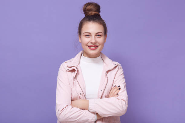 portrait of modest young woman expressing positive emotions, posing isolated over lilac background, keeping hands folded, standing with big hair bun, looking directly at camera. people concept. - unwillingness imagens e fotografias de stock