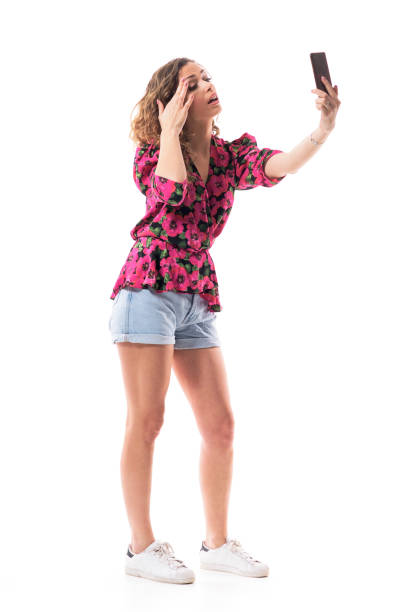 istock Young trendy woman adjusting eyebrow make up using cell phone screen as mirror 1215565899