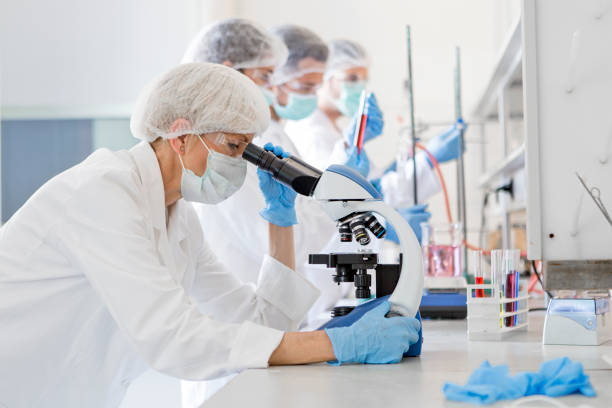 Scientists studying a virus ,looking through microscope Scientists in protective suits in a science laboratory study a virus research stock pictures, royalty-free photos & images