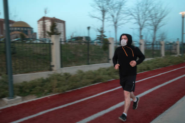 Isolated young man wearing mask and a hoodie running at a park stock photo