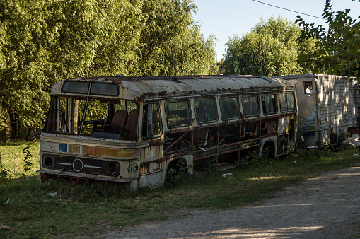 Broken-down rusted bus standing on the side of a gravel road