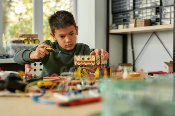 istock Taking You Forward. Boy using screwdriver while fixing bolts on a robot vehicle. Smart kids and STEM education. 1215569542