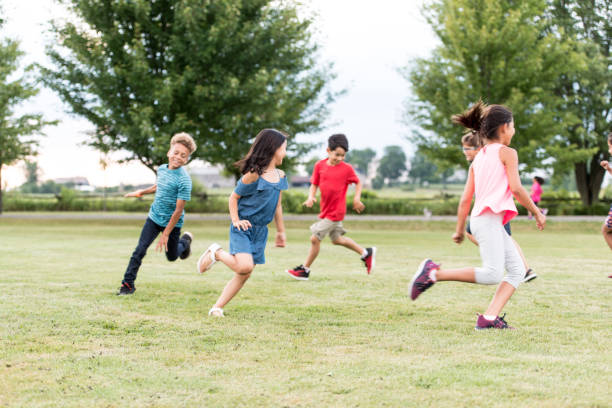 Elementary School Students Play at Recess stock photo A multi-ethnic group of elementary school students play tag outside at recess.  They are running around the grass outside of the school. schoolyard stock pictures, royalty-free photos & images