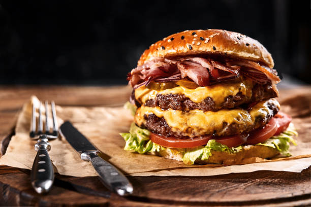 hamburguesa fresca y jugosa sobre una almohada de papel con cerveza sobre una mesa de madera. fondo oscuro, comida americana tradicional. comida basura - fine wood fotografías e imágenes de stock