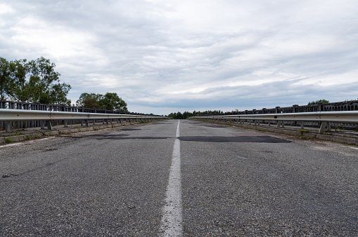 Asphalt road on the bridge. Asphalt road with patches. Leading road with a strip. Horizon and clouds.