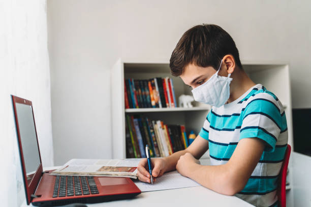 istock Cute boy with face protective mask studying at home. Online education. Coronavirus epidemic 1215572281
