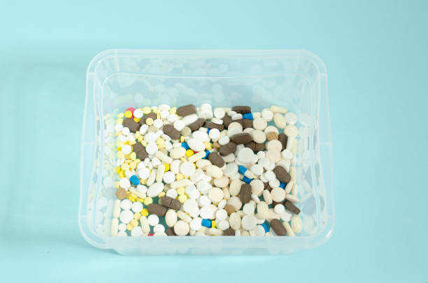 istock Container with pills. Multicolored and white pills in a transparent box. Pills on a blue background. 1215574116