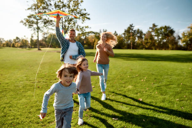 There are no words to describe how special kids are. Happy family playing a kite. Outdoor family weekend Portrait of cheerful parents with two kids running with kite in the park on a sunny day. Family, kids and nature concept. Horizontal shot. weekend activities stock pictures, royalty-free photos & images