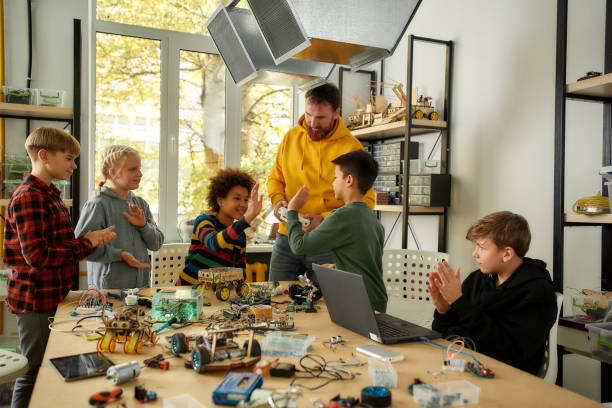 istock We Did It. Young technicians are happy with the result of their work, giving high five. Creative male teacher holding console controller. Science and education. 1215578063