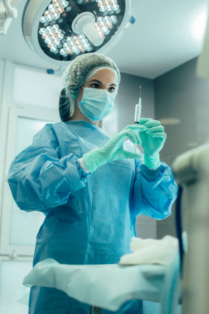 joven enfermera cuidadosa en la operación quirúrgica foto de stock - syringe medical injection surgical needle surgical mask fotografías e imágenes de stock