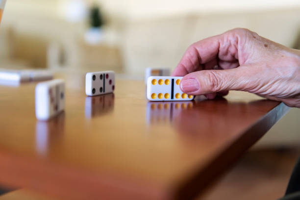 A close-up view of a retired senior woman who is playing domino games at home with his husband. An older senior couple is playing a board game in the living room of their apartment.