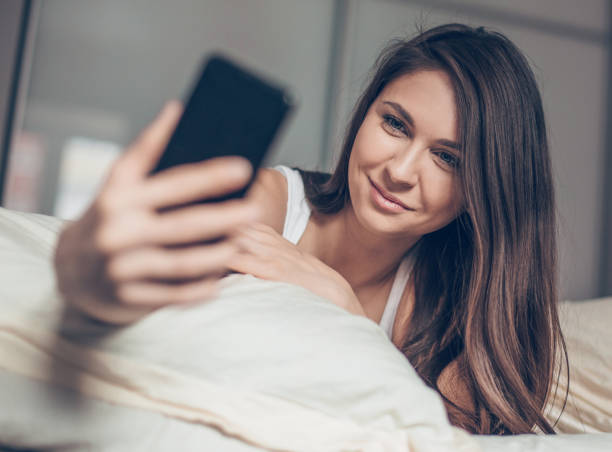 istock Cute young woman lying on the bed and make a selfie 1215581241