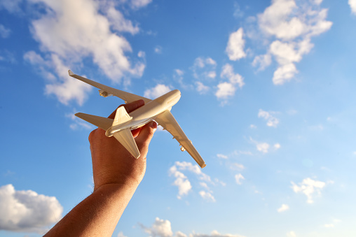 Toy airplane model in a man's hand on a background of the sky with clouds. Man holding airplane in hands and flying over the cloudy blue sky background. Travel and flight concept. Travel photography motivator for vacation.
