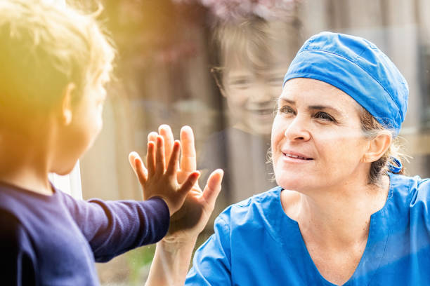 Mature Healthcare worker posing seeing her son with a window glass separating them to avoid possible contagion Caucasian Mature Healthcare worker posing seeing her son with a window glass separating them to avoid possible contagion female nurse photos stock pictures, royalty-free photos & images