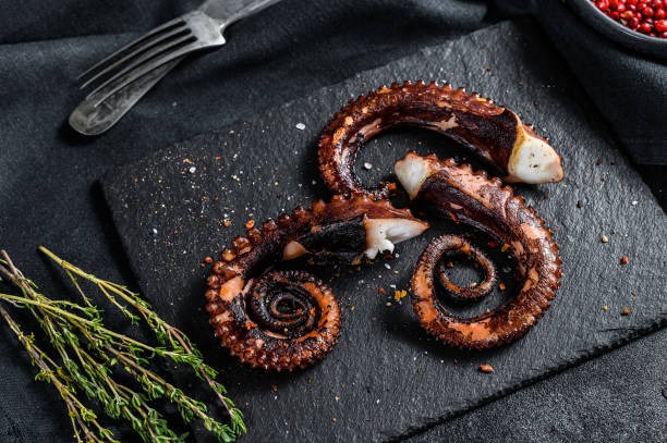 istock Fried octopus tentacles with thyme and pink pepper. Fresh seafood. Black background. Top view 1215582221