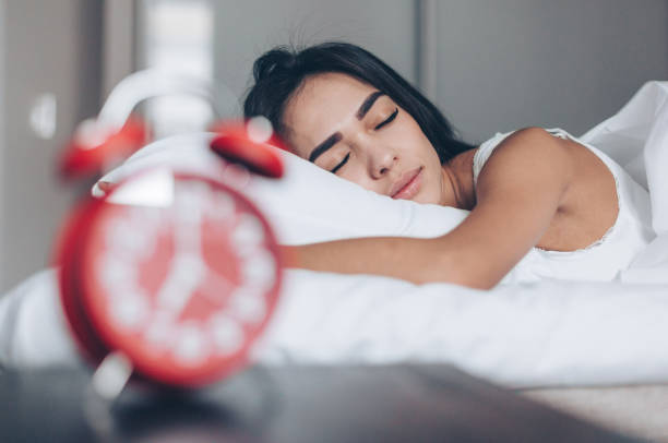 istock Young woman sleeping on bed. Red alarm clock at foreground 1215582798