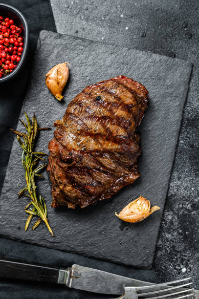 istock Grilled Flat Iron steak on a stone Board, marbled beef. Black background. Top view 1215584822