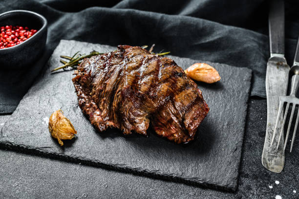 istock Grilled Top Blade steak on a stone Board, marbled beef. Black background. Top view 1215584892