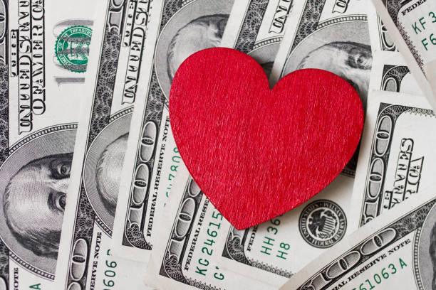 red wooden heart and many greenbacks one hundred dollar dollars with image of franklin scattered on the surface - greenbacks imagens e fotografias de stock